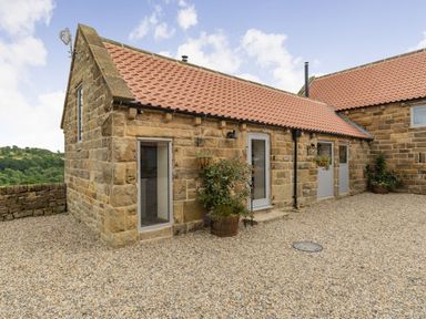 A stone building with a tiled roof and gravel ground with potted plants outside at Foxglove in Goathland