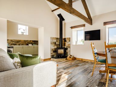 A living room with a sofa, wood stove, dining table, and kitchen area at Foxglove Goathland
