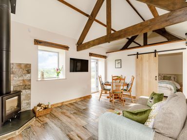 A living room with wooden beams a wood stove a dining table and chairs and a sofa at Foxglove in Goathland