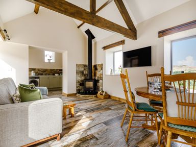A living room with a couch dining table wood stove and exposed beams at Foxglove in Goathland