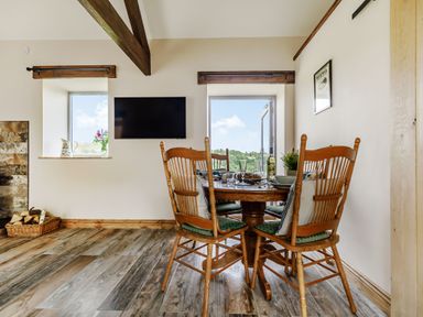 A dining area with a wooden table and four chairs near windows and a wall-mounted television at Foxglove Goathland