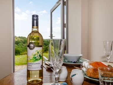 A bottle of elderflower wine on a wooden table with glasses plates bread and cutlery near an open door showing an outdoor view at Foxglove in Goathland