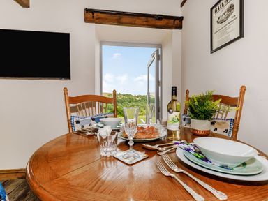 A dining table set with plates forks glasses wine and a plant near an open door showing a green landscape at Foxglove in Goathland