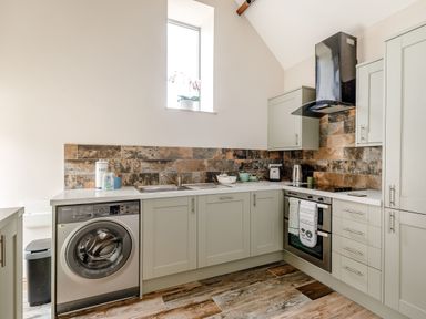 A kitchen with light green cabinets washing machine oven and a window with a plant at Foxglove in Goathland