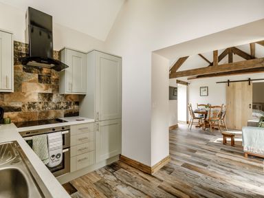 A kitchen with cabinets and a stove connected to a dining area with wooden chairs and exposed ceiling beams at Foxglove in Goathland