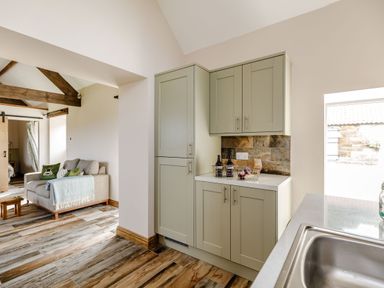 A kitchen with green cabinets and a living room with a sofa and wooden beams at Foxglove in Goathland
