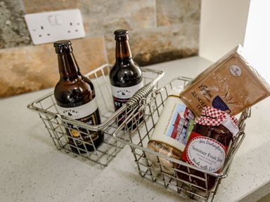 Two metal baskets on a countertop with two bottles in one and jam biscuits and tea bags in the other at Foxglove in Goathland