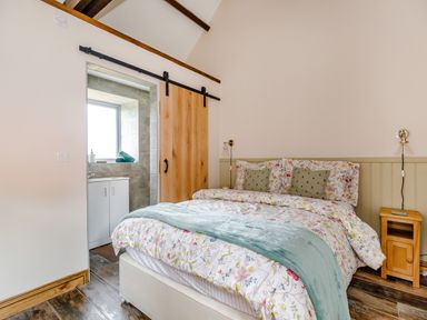 A bedroom with a bed floral bedding wooden bedside table and a sliding wooden door leading to a bathroom at Foxglove in Goathland