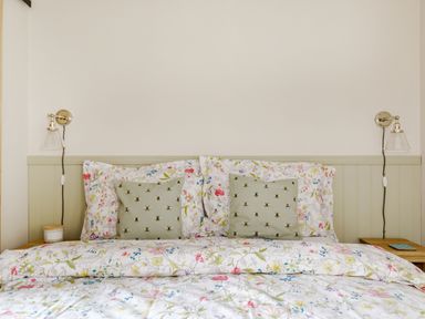 A bed with floral bedding and bee-printed cushions with wall lamps on each side at Foxglove in Goathland