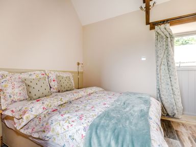 A bedroom with a double bed floral bedding teal throw two green cushions wall light curtains and wooden ceiling beam at Foxglove in Goathland