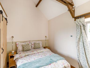 A bedroom with floral bedding two bedside tables wooden beams and floral curtains at Foxglove in Goathland