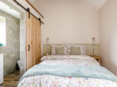 A bedroom with a bed covered in floral bedding and a sliding wooden door leading to a tiled bathroom at Foxglove in Goathland
