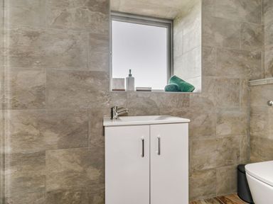 A bathroom sink cabinet with a faucet below a window with towels and soap dispenser on the sill at Foxglove in Goathland
