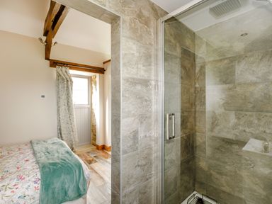 A bedroom with floral bedding and green throw next to a tiled shower with glass door at Foxglove in Goathland