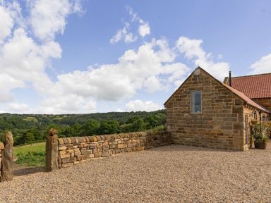 A stone building with a gravel courtyard and a low stone wall overlooking green hills and trees at Foxglove in Goathland
