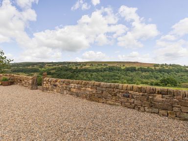 An outdoor gravel area with a stone wall overlooking a green countryside landscape at Foxglove in Goathland
