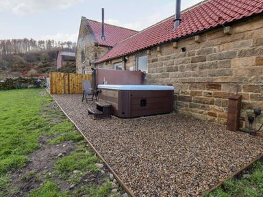 An outdoor area with a hot tub and chair on a gravel surface next to a stone building with a red tiled roof at Foxglove in Goathland