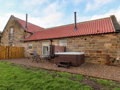 A stone house with a red tiled roof patio furniture and a hot tub on a gravel area at Foxglove in Goathland