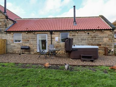 A stone house with a red tiled roof a patio with chairs table and a barbecue and a hot tub on a grassy yard at Foxglove in Goathland