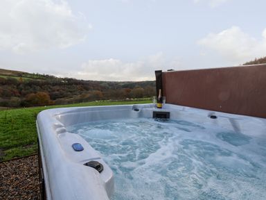 An outdoor hot tub on grass with a bottle and two glasses with a countryside view at Foxglove in Goathland
