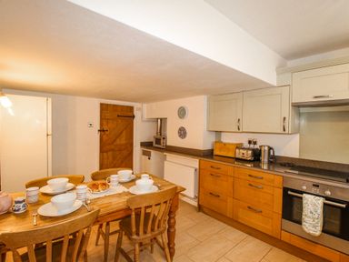 A kitchen with wooden dining table and chairs and wooden cabinets at Cajun Cottage in West Lulworth