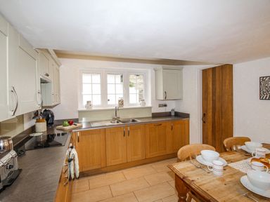 A kitchen with wooden cabinets and a dining table set with bowls and mugs at Cajun Cottage in West Lulworth