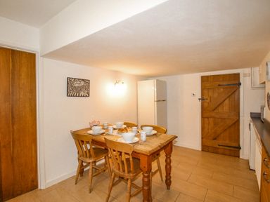 A dining area with a wooden table set for four near a white refrigerator and wooden door at Cajun Cottage in West Lulworth