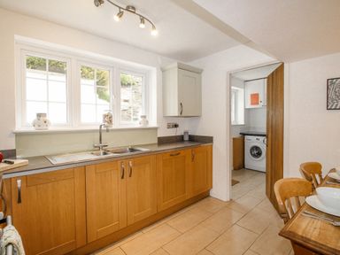 A kitchen with wooden cabinets a double sink and a view into a laundry room with a washing machine at Cajun Cottage West Lulworth
