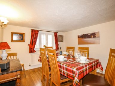 A dining room with a wooden table covered with a red plaid tablecloth and six wooden chairs at Cajun Cottage in West Lulworth
