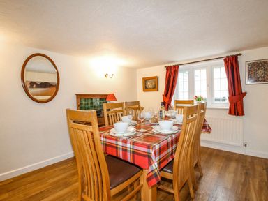 A dining room with a wooden table set for six with a red plaid tablecloth and wooden chairs at Cajun Cottage in West Lulworth