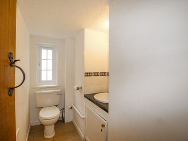 A small bathroom with a toilet next to a window and a sink with a cabinet in Cajun Cottage West Lulworth