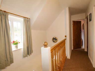 A hallway with a wooden railing a window with curtains and flowers on the sill at Cajun Cottage in West Lulworth