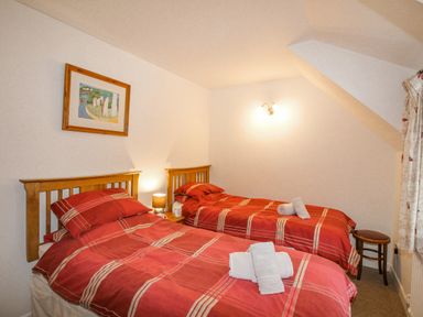 A bedroom with two single beds with red striped bedding and towels on beds at Cajun Cottage in West Lulworth