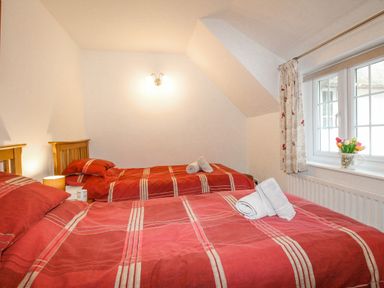 A bedroom with two single beds with red and beige striped bedding a window with curtains and a vase of flowers on the windowsill at Cajun Cottage in West Lulworth