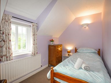 A small bedroom with a single bed bedside table lamp and a wooden chest of drawers at Cajun Cottage in West Lulworth