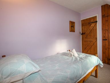 A bedroom with a single bed with blue patterned bedding and rolled towels on top a wooden door and closet at Cajun Cottage in West Lulworth
