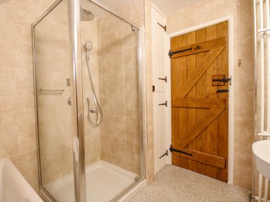 A bathroom with a glass shower enclosure wooden door and a white sink at Cajun Cottage in West Lulworth