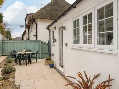 An outdoor patio with table and chairs next to a white house with windows at Cajun Cottage in West Lulworth