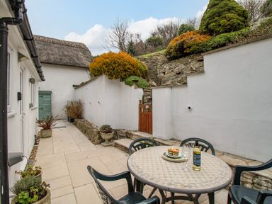 An outdoor patio with a tiled round table and black chairs by white walls and stone steps at Cajun Cottage in West Lulworth