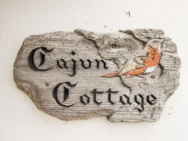 A wooden sign with the words Cajun Cottage and a painted bird on it