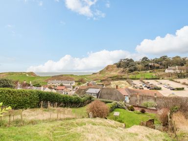 A hillside view over thatched cottages parked cars and green fields at Cajun Cottage in West Lulworth