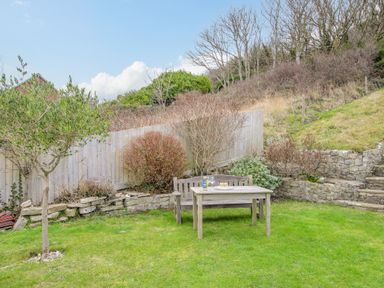 A garden with a wooden bench and table on grass and a small tree at Cajun Cottage in West Lulworth