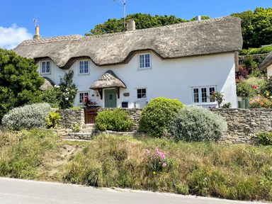A thatched roof cottage with white walls and a stone wall garden in front at Cajun Cottage in West Lulworth