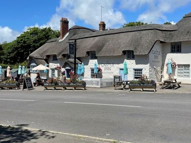 A thatched roof pub with outdoor seating and umbrellas on a sunny day at Cajun Cottage in West Lulworth