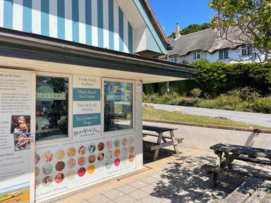 An outdoor ice cream parlor with a menu and picnic tables near a road with houses in the background at Cajun Cottage in West Lulworth