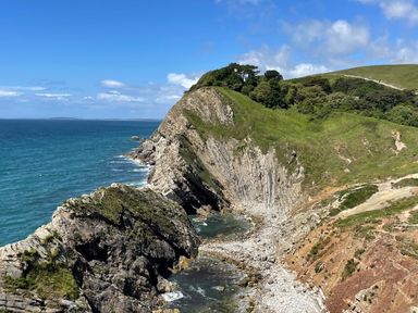 A rocky coastal cliff with green vegetation beside a blue sea at Cajun Cottage in West Lulworth