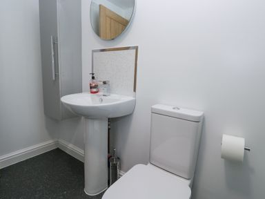 A bathroom with a pedestal sink a wall-mounted cabinet a round mirror a toilet and a toilet paper holder at Eildon Lodge in Gosforth