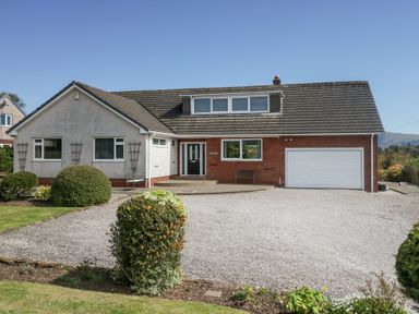 A detached house with a gravel driveway and garden shrubs at Eildon Lodge in Gosforth
