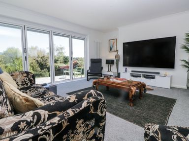 A living room with patterned sofas a wooden coffee table a large wall-mounted TV and sliding glass doors at Eildon Lodge in Gosforth