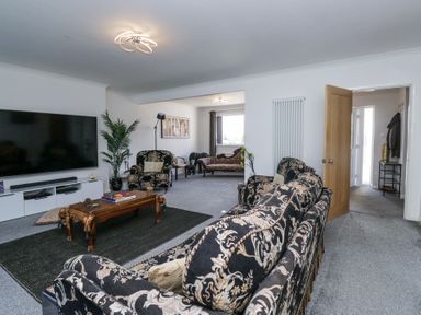 A living room with patterned sofas a wooden coffee table a large television and an open doorway at Eildon Lodge in Gosforth